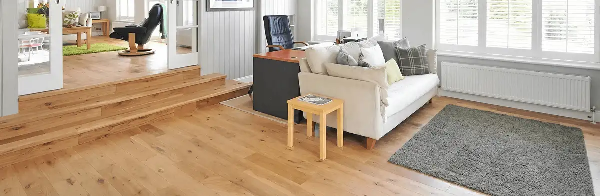 A modern living room with professionally installed laminate flooring, a beige sofa, a small side table, a gray rug, and large windows with white shutters in Jackson, MS
